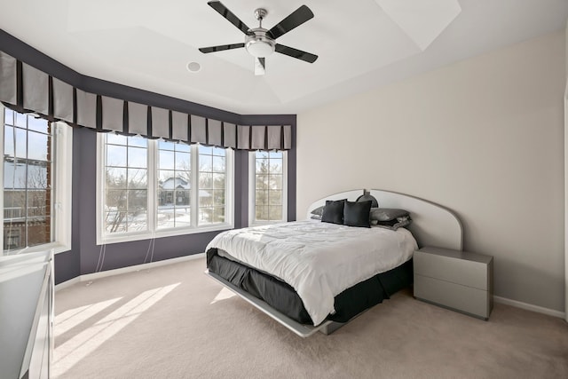 carpeted bedroom featuring ceiling fan, a tray ceiling, and baseboards