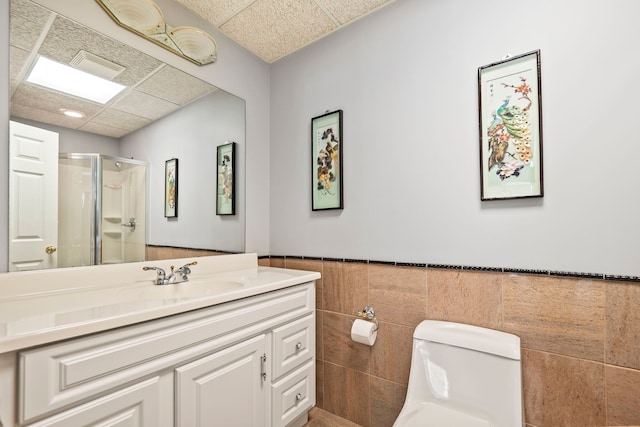 full bathroom featuring a stall shower, a drop ceiling, toilet, a wainscoted wall, and vanity