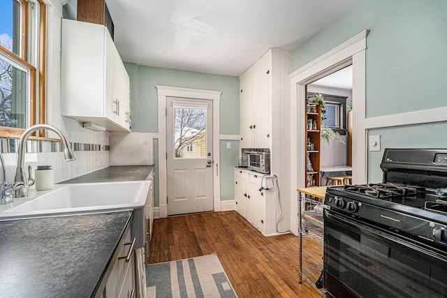 kitchen featuring dark wood-type flooring, a sink, white cabinetry, dark countertops, and black gas range oven