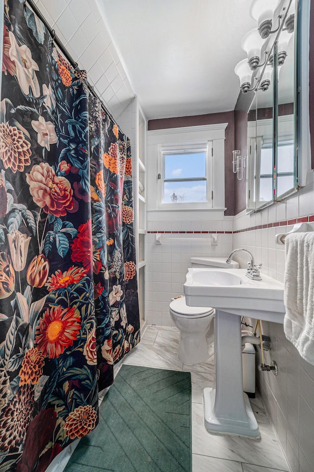 full bathroom featuring wainscoting, toilet, and tile walls