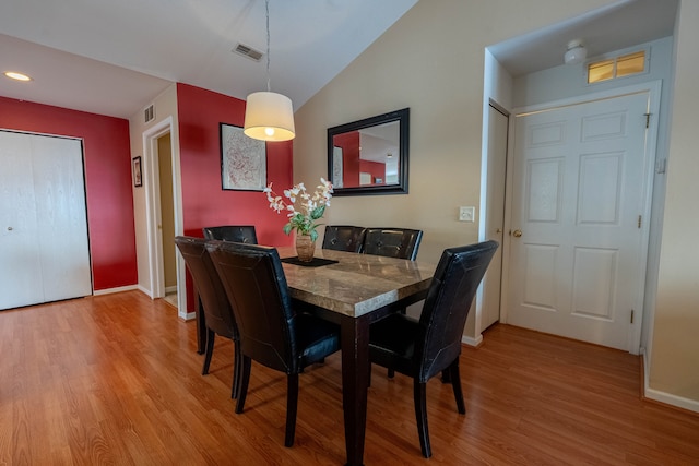 dining space with vaulted ceiling, light wood-type flooring, visible vents, and baseboards