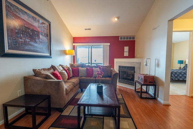 living area featuring a fireplace, visible vents, vaulted ceiling, and wood finished floors