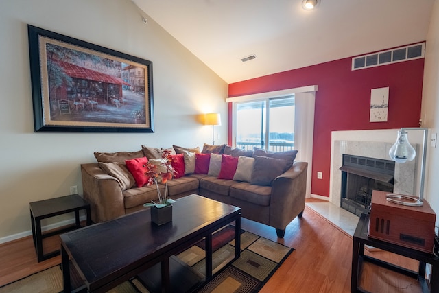 living room featuring a high end fireplace, visible vents, vaulted ceiling, and wood finished floors