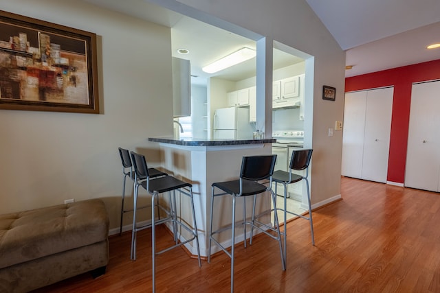 kitchen with under cabinet range hood, a peninsula, white appliances, wood finished floors, and a kitchen bar