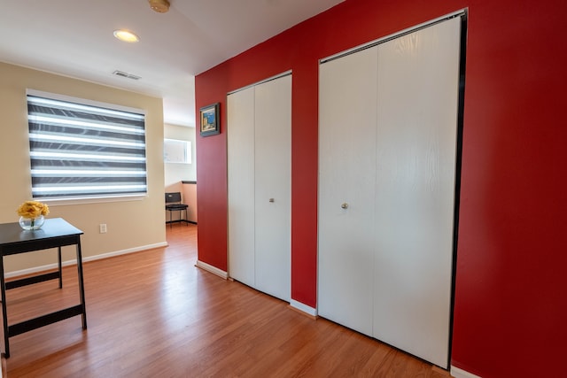 hall with wood finished floors, visible vents, and baseboards