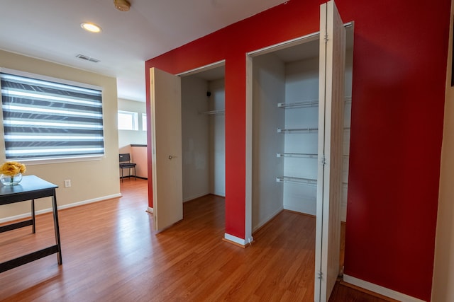 corridor featuring light wood-style flooring, visible vents, and baseboards