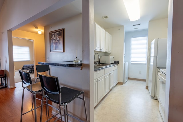 kitchen with white appliances, visible vents, dark countertops, a kitchen bar, and a sink