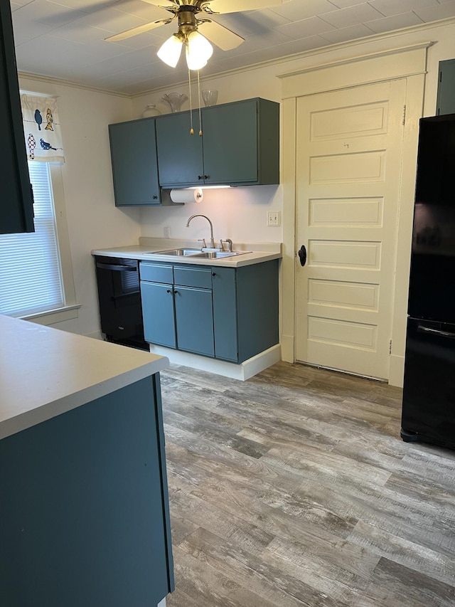 kitchen featuring a sink, light countertops, light wood-type flooring, black appliances, and crown molding