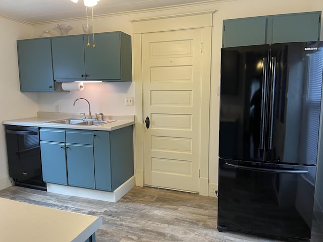 kitchen with a sink, light countertops, light wood-type flooring, black appliances, and crown molding