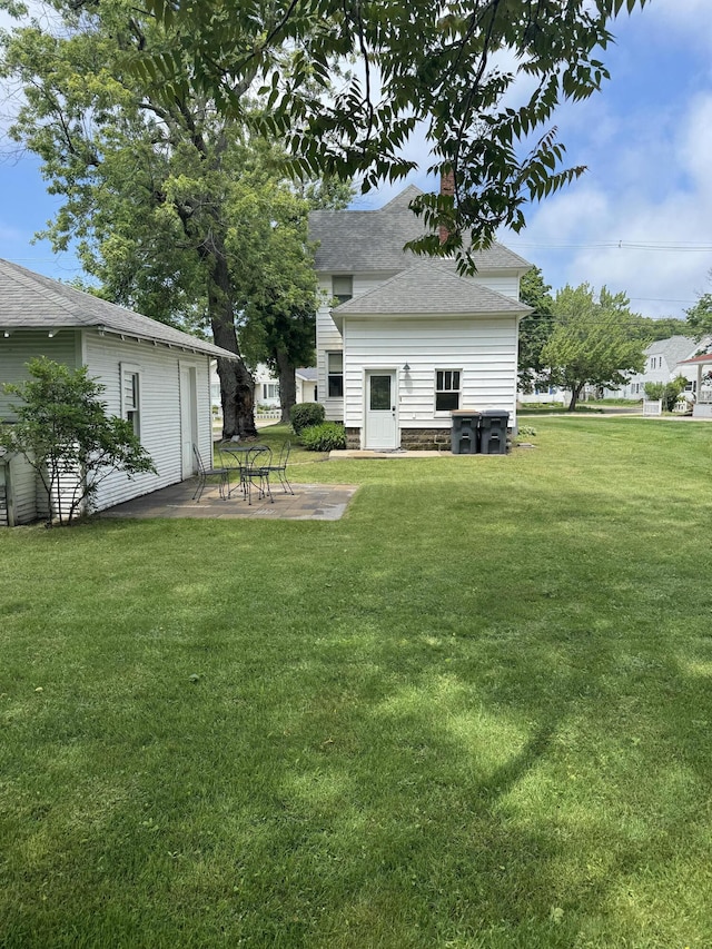 rear view of property with roof with shingles, a chimney, a lawn, and a patio