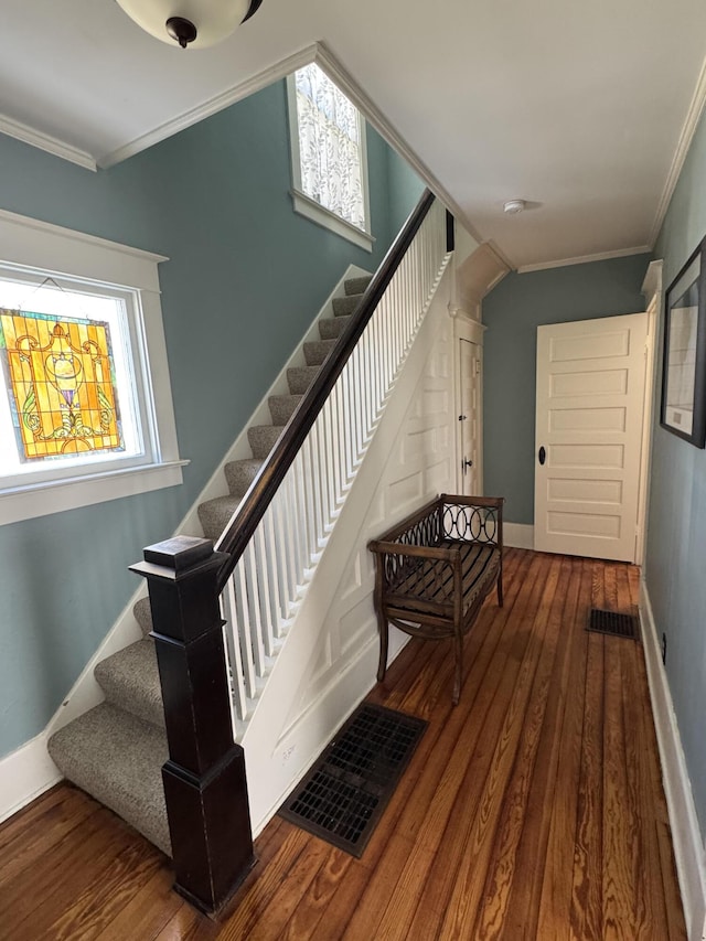 stairs with ornamental molding, wood finished floors, visible vents, and baseboards