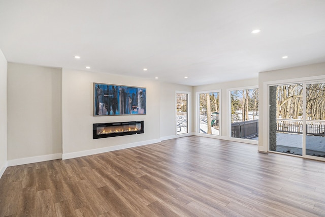 unfurnished living room featuring recessed lighting, a glass covered fireplace, light wood-style flooring, and baseboards