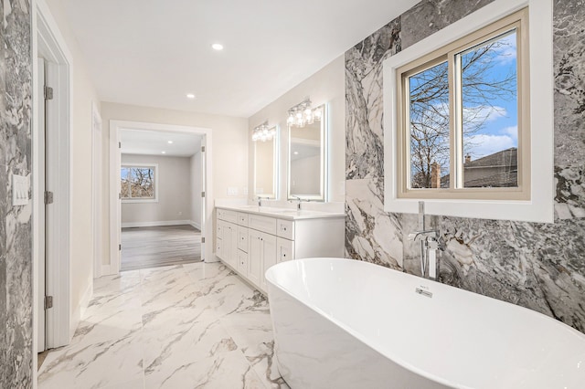 full bath featuring marble finish floor, double vanity, recessed lighting, a freestanding bath, and a sink