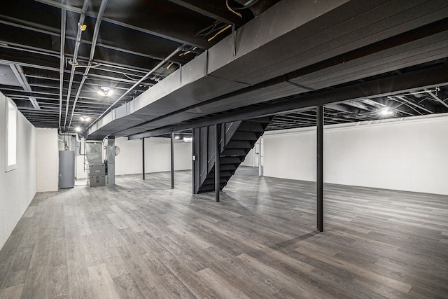 finished basement with heating unit, stairs, gas water heater, and wood finished floors