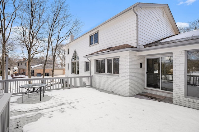 snow covered house with brick siding, a chimney, and a wooden deck