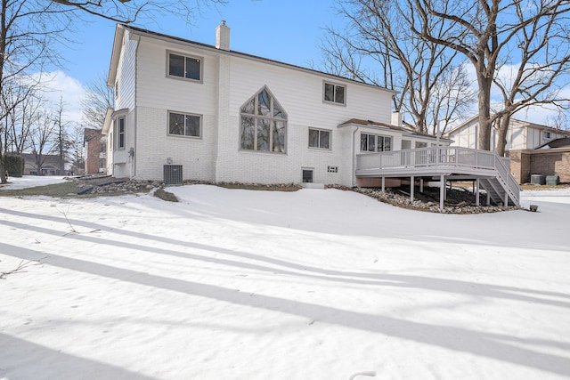 snow covered rear of property featuring a chimney, stairway, a deck, central AC, and brick siding