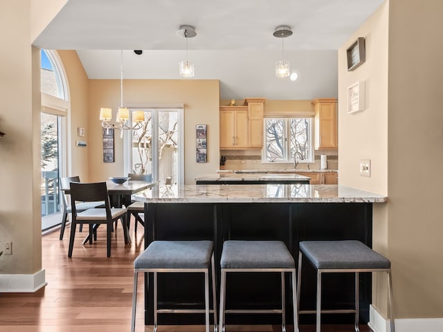 kitchen with a kitchen bar, light brown cabinets, a sink, backsplash, and wood finished floors