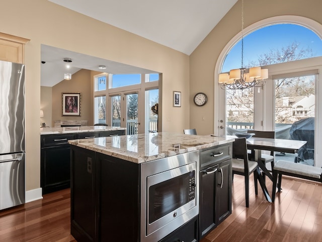 kitchen with appliances with stainless steel finishes, a kitchen island, dark wood-type flooring, and dark cabinets