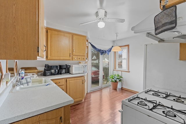 kitchen featuring white appliances, a sink, light countertops, light wood-type flooring, and range hood