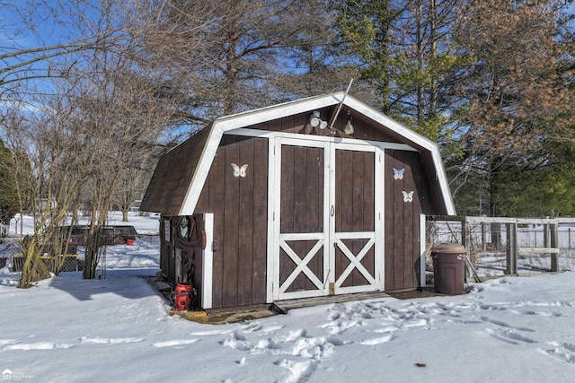 snow covered structure with a storage shed, fence, and an outdoor structure