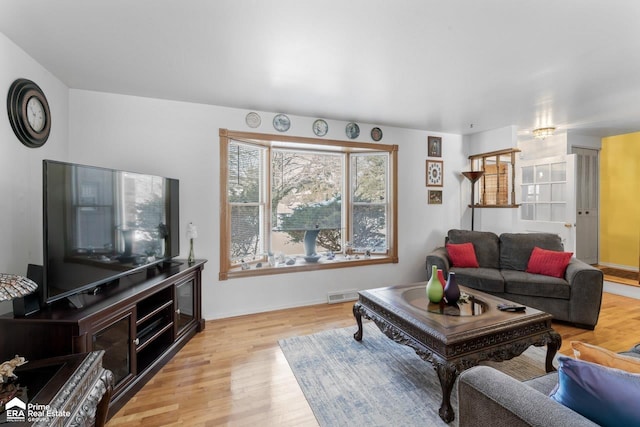 living room with light wood-style flooring, visible vents, and baseboards