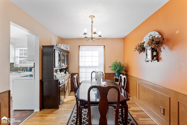 dining space featuring light wood-style floors, plenty of natural light, a notable chandelier, and wainscoting