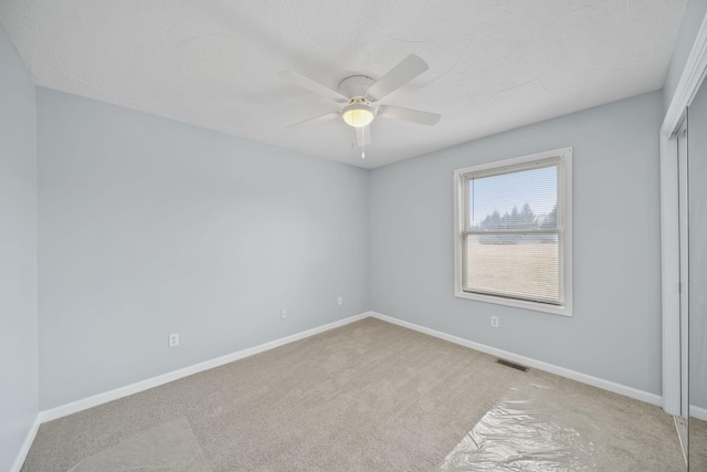 unfurnished room with a ceiling fan, visible vents, light carpet, and baseboards