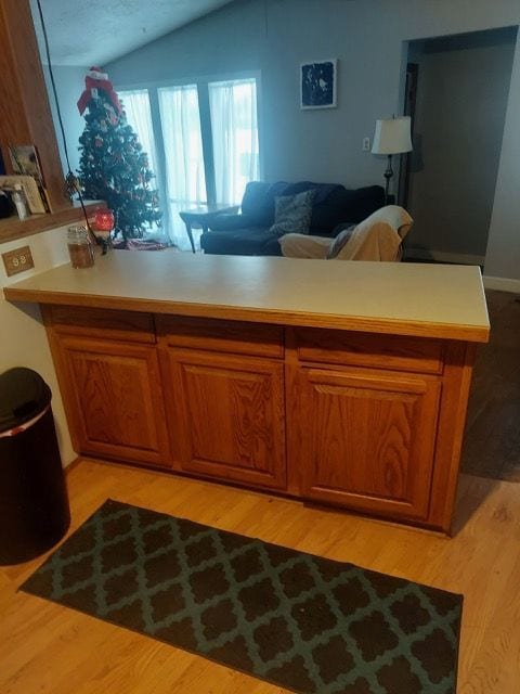 kitchen with brown cabinets, lofted ceiling, light countertops, open floor plan, and light wood-type flooring