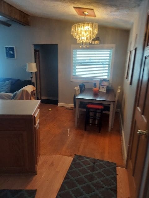 dining space featuring a chandelier, a textured ceiling, baseboards, and wood finished floors