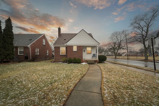 bungalow featuring brick siding, a front lawn, a chimney, and fence