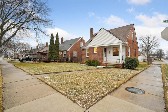 bungalow-style house featuring a residential view, a chimney, a front lawn, a porch, and brick siding