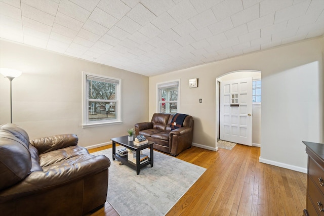 living area featuring arched walkways, baseboards, and light wood finished floors