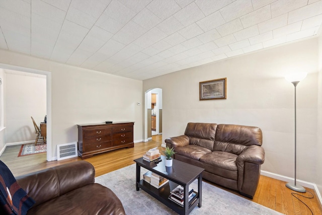 living area with baseboards, visible vents, arched walkways, and wood finished floors