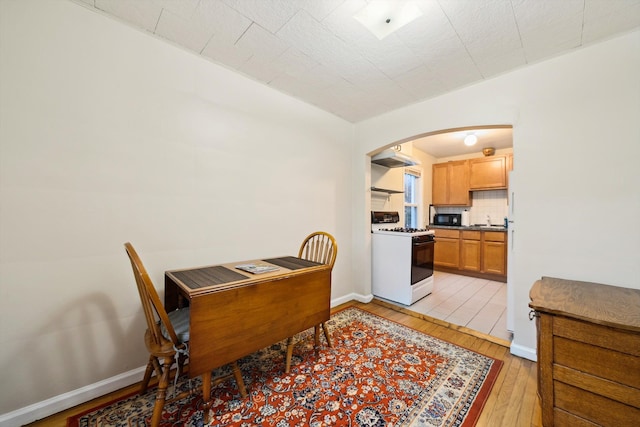 dining area with light wood-type flooring, baseboards, and arched walkways