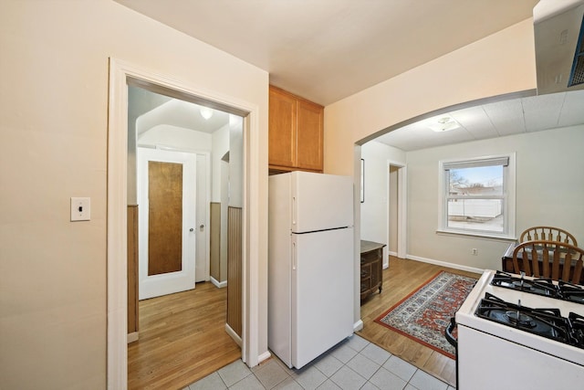 kitchen with arched walkways, white appliances, light wood-type flooring, and baseboards