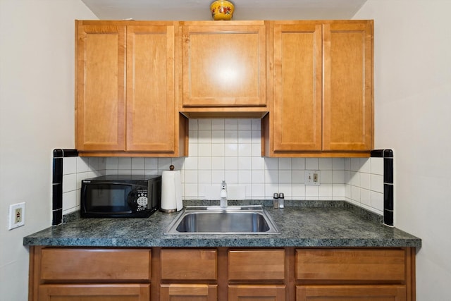 kitchen featuring dark countertops, black microwave, a sink, and backsplash