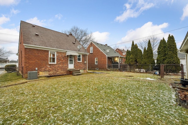 rear view of house with entry steps, central AC unit, a fenced backyard, a yard, and brick siding