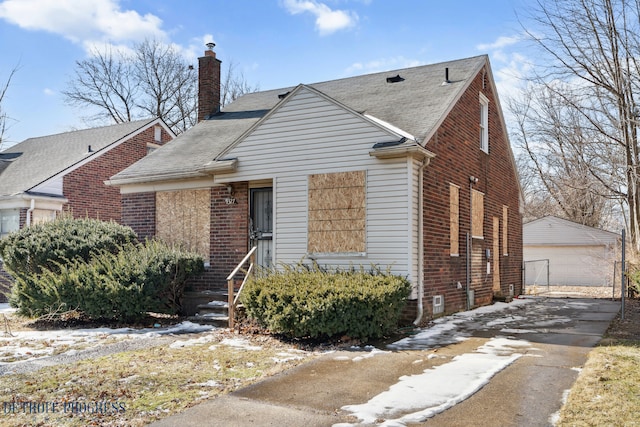 view of front facade featuring brick siding, a chimney, an outdoor structure, and a detached garage