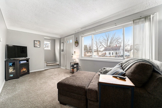 carpeted living area featuring a warm lit fireplace, baseboards, and a textured ceiling