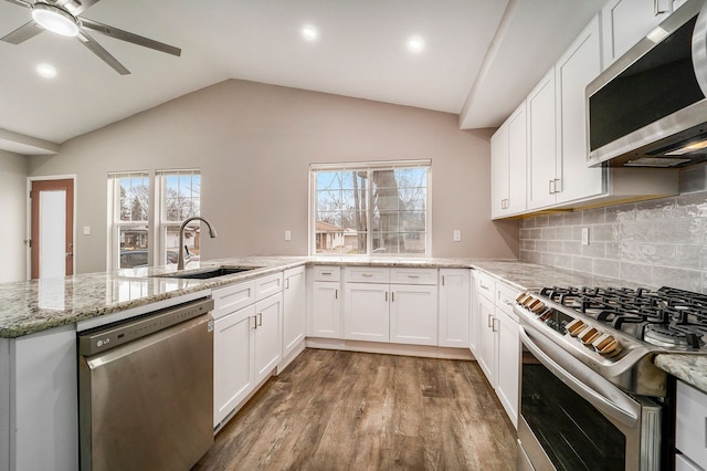 kitchen with white cabinets, appliances with stainless steel finishes, a peninsula, light stone countertops, and a sink