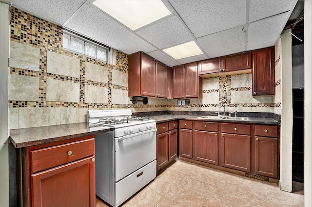 kitchen with a paneled ceiling, a sink, decorative backsplash, gas range gas stove, and dark countertops