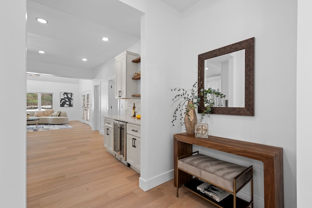 corridor with light wood-style floors, wine cooler, baseboards, and recessed lighting