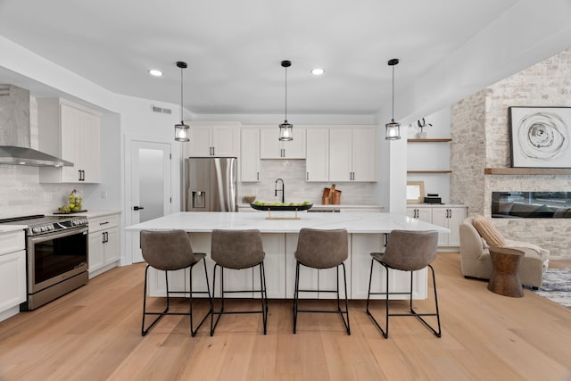 kitchen featuring wall chimney range hood, white cabinetry, appliances with stainless steel finishes, and light wood-style floors