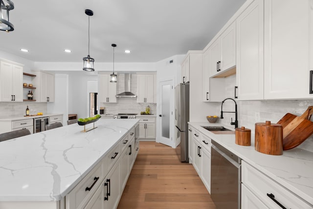 kitchen featuring open shelves, stainless steel appliances, white cabinetry, a sink, and wall chimney range hood