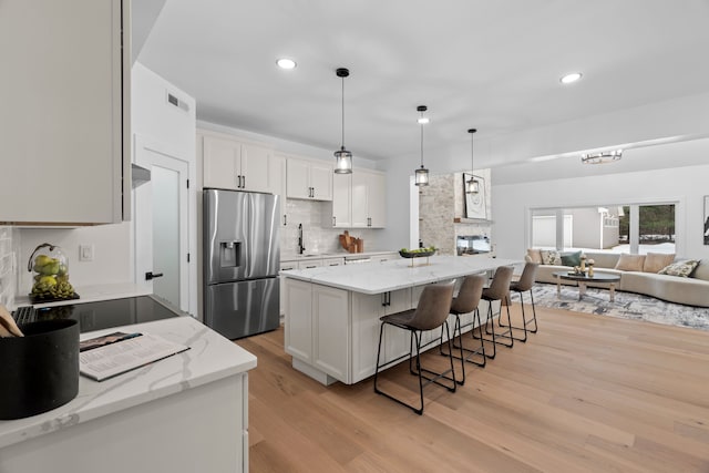 kitchen with a sink, a kitchen breakfast bar, open floor plan, light wood-style floors, and stainless steel fridge