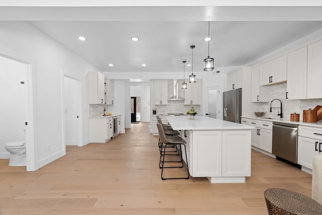 kitchen featuring stainless steel appliances, light wood-style floors, white cabinets, light countertops, and wall chimney exhaust hood