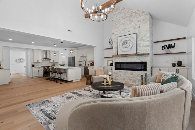 living room with high vaulted ceiling, a stone fireplace, visible vents, light wood finished floors, and an inviting chandelier