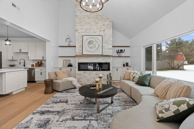 living room with a chandelier, high vaulted ceiling, a large fireplace, visible vents, and light wood finished floors