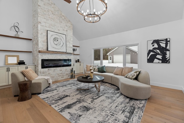 living area featuring a chandelier, high vaulted ceiling, a stone fireplace, wood finished floors, and baseboards