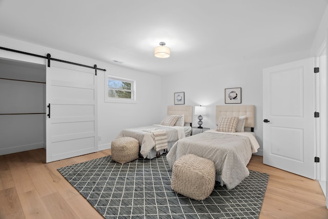 bedroom with visible vents, light wood-style flooring, baseboards, and a barn door